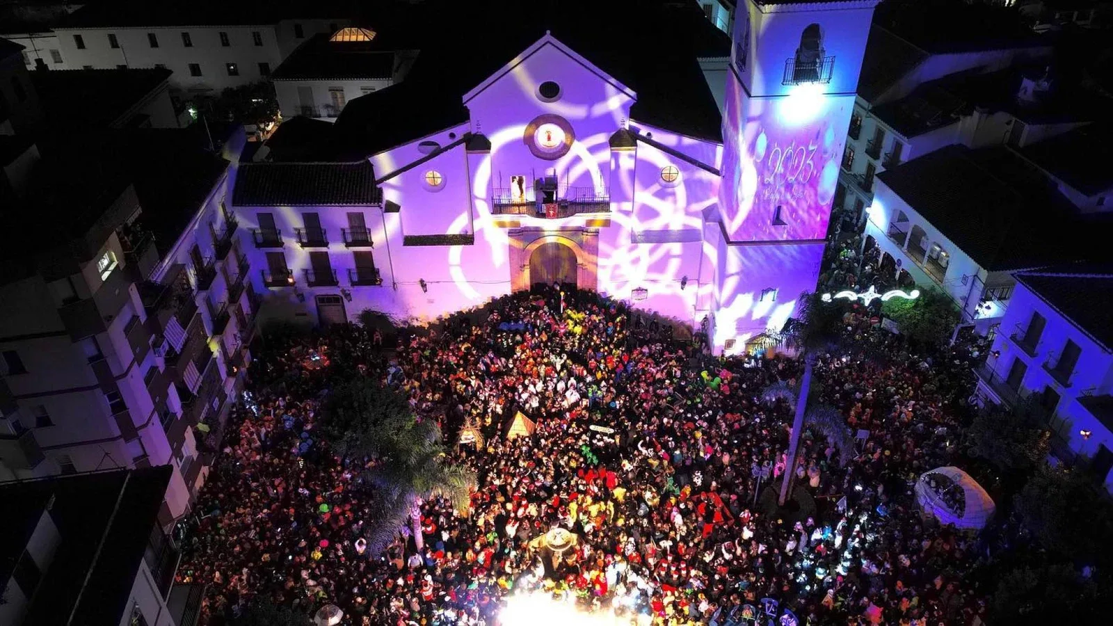 Vista aérea de una noche de fiesta en Coín: la plaza llena de gente ante la iglesia de San Juan Bautista iluminada