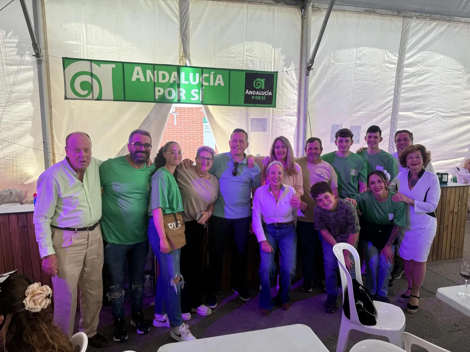 Militantes y simpatizantes de Andalucía Por Sí de todas las edades, abrazados bajo una pancarta del partido en una caseta
