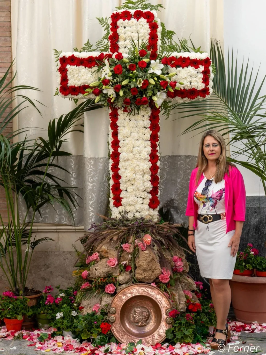 Cristina RJ Osorio junto a una cruz de claveles rojos y blancos