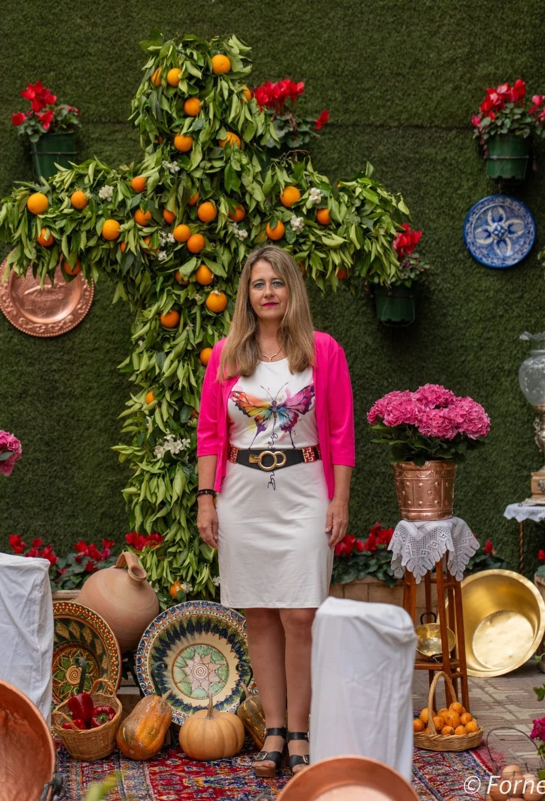 Cristina RJ Osorio ante una cruz de flores y naranjas
